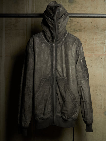 A distressed, dark gray leather hooded jacket with a front zipper, hanging on a black metal rack against a textured concrete wall.