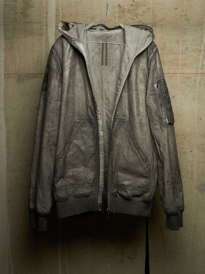 A distressed, washed-out gray hooded jacket hanging on a wire hanger against a textured concrete wall.