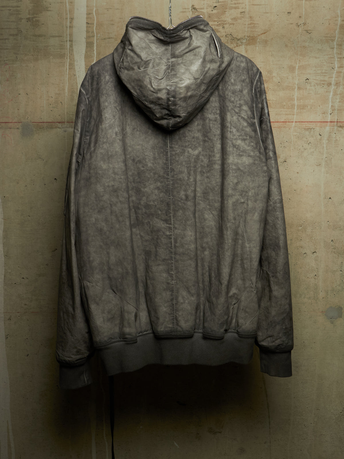 A dark gray, acid-washed hooded sweatshirt hanging against a textured concrete wall.