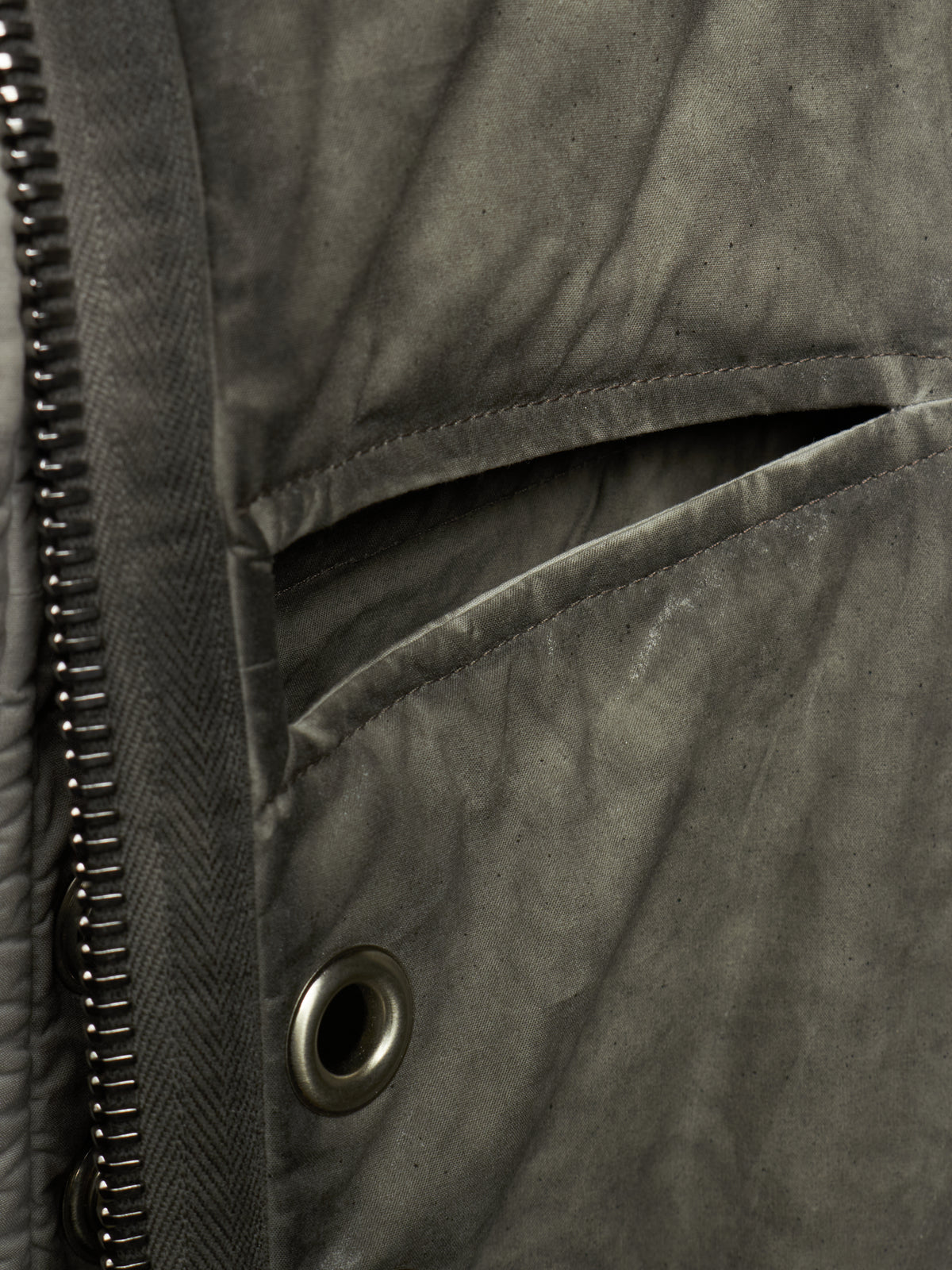 Close-up detail of a dark gray quilted jacket showing a zippered pocket, metal snap button, and textured fabric.