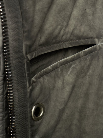 Close-up detail of a dark gray quilted jacket showing a zippered pocket, metal snap button, and textured fabric.