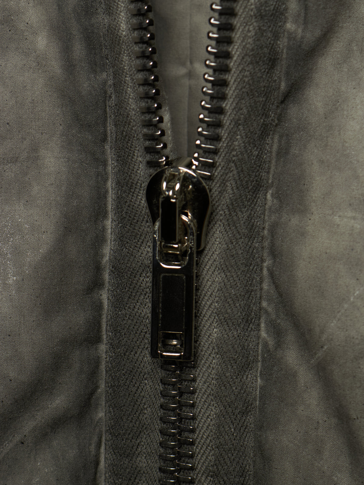 Close-up of a dark gray textured fabric jacket with a black metal zipper running vertically down the center.