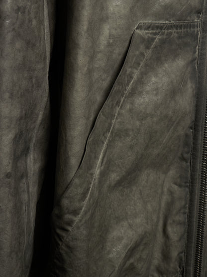 Close-up of a dark gray suede or nubuck jacket fabric, showing the textured material and a zippered pocket.