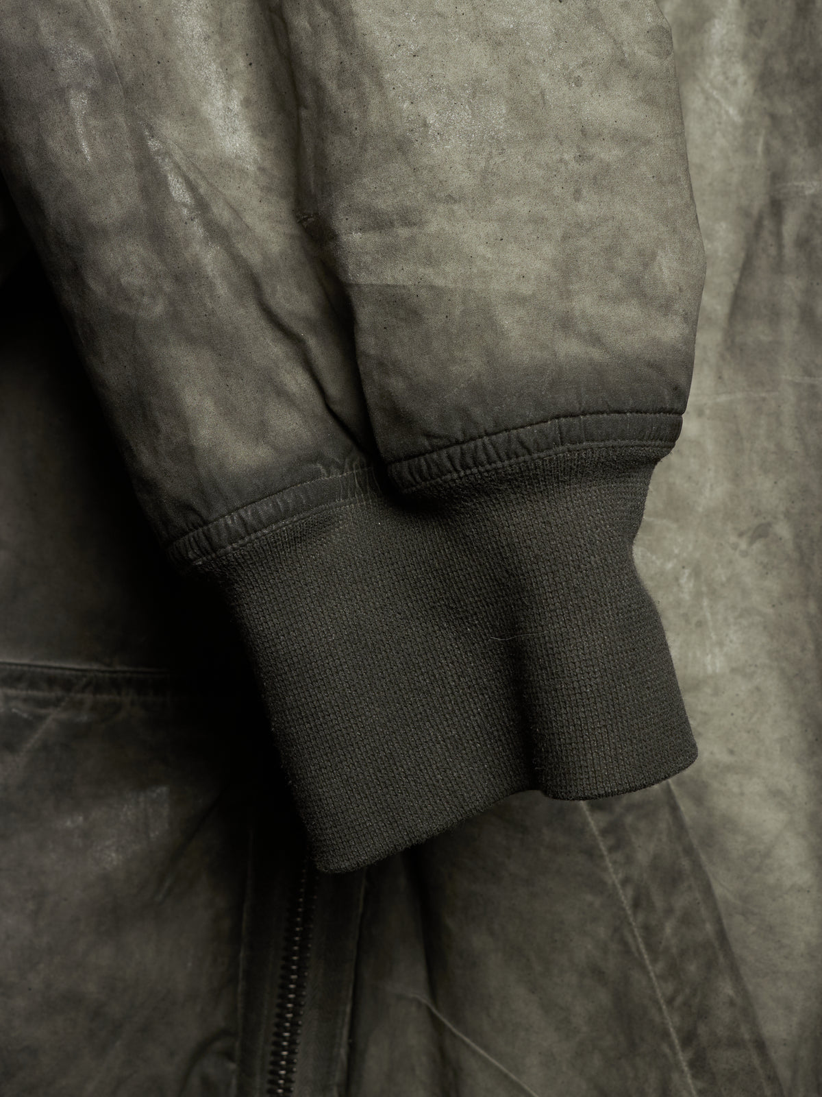 Close-up detail of a dark gray suede or nubuck jacket sleeve with ribbed knit cuff and a zipper seam.
