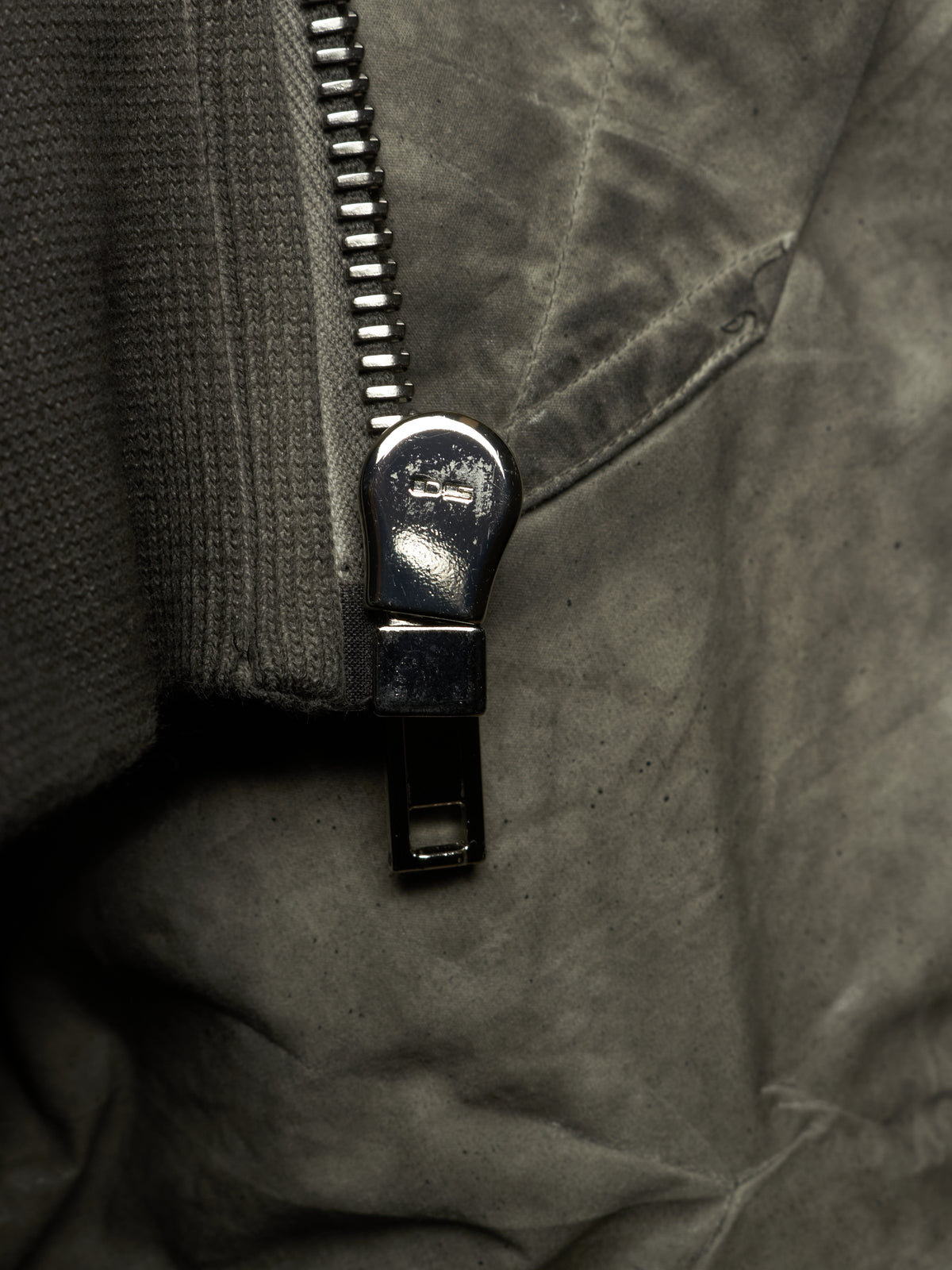 Close-up of a dark gray zippered garment with a black metal zipper pull and textured fabric.