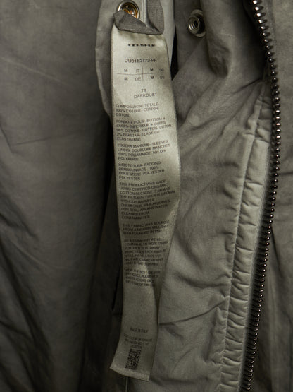 Close-up of a gray quilted jacket with a sewn-in size and care label visible, next to a metal zipper.