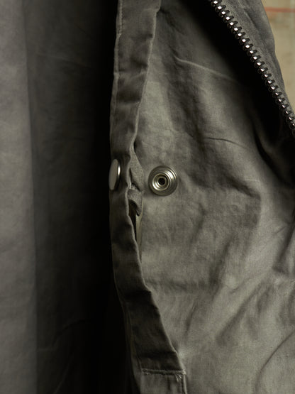 Close-up detail of a dark gray jacket showing a metal snap button, zipper teeth, and textured fabric.