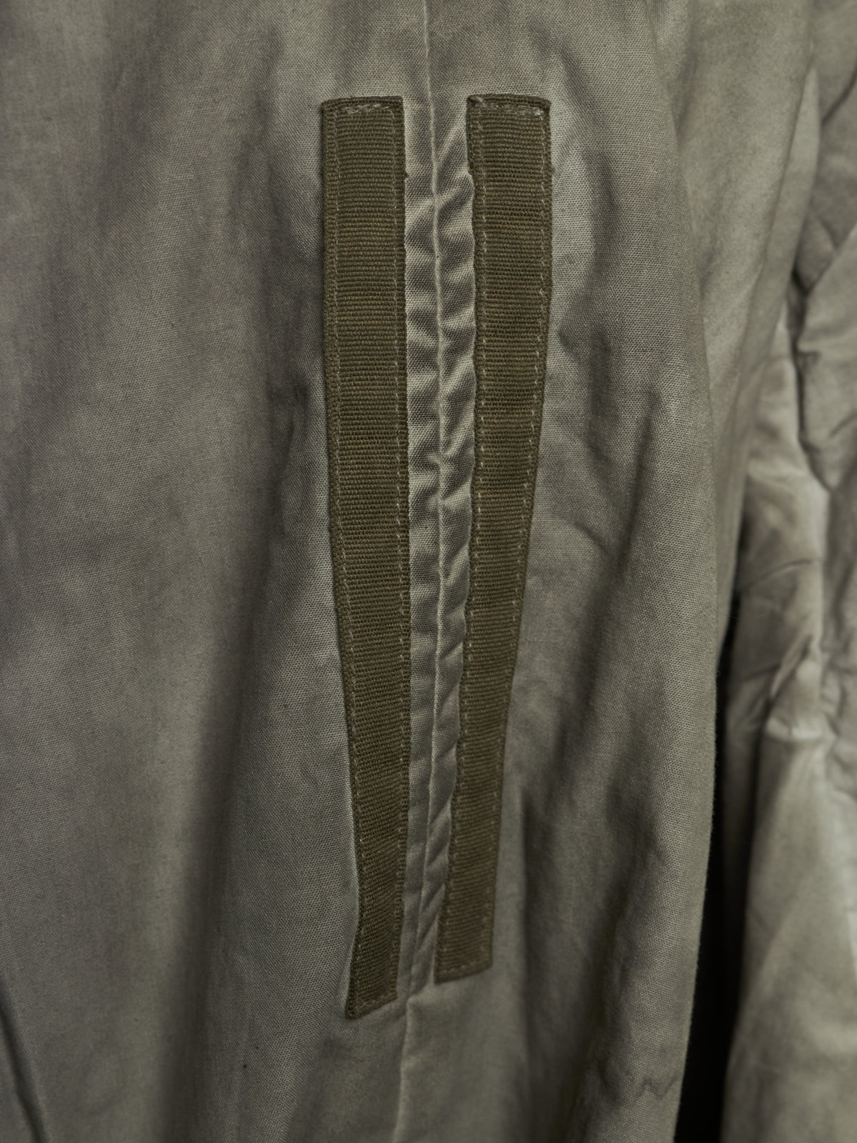 Close-up of a gray fabric garment featuring two vertical olive green hook-and-loop strap details on the front.