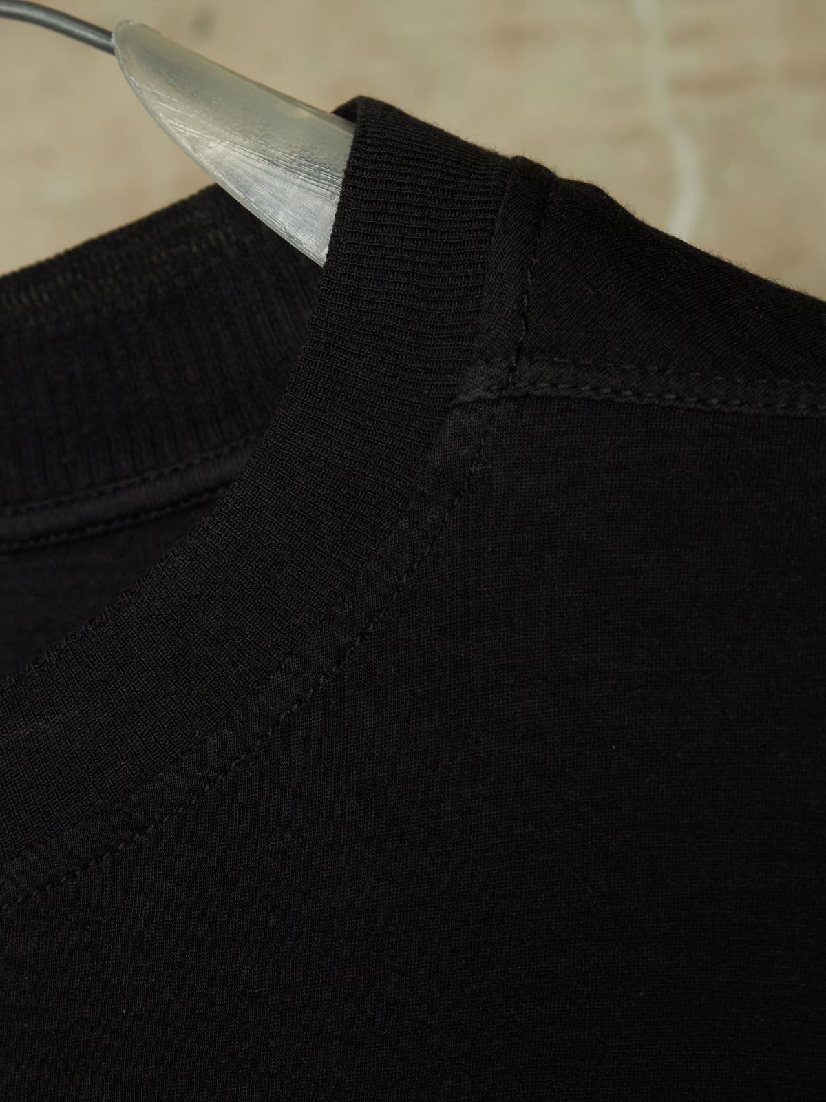 Close-up detail of a black ribbed knit crewneck sweater on a clear plastic hanger, showing the collar stitching and texture.