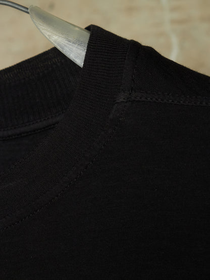 Close-up detail of a black ribbed knit crewneck sweater on a clear plastic hanger, showing the collar stitching and texture.