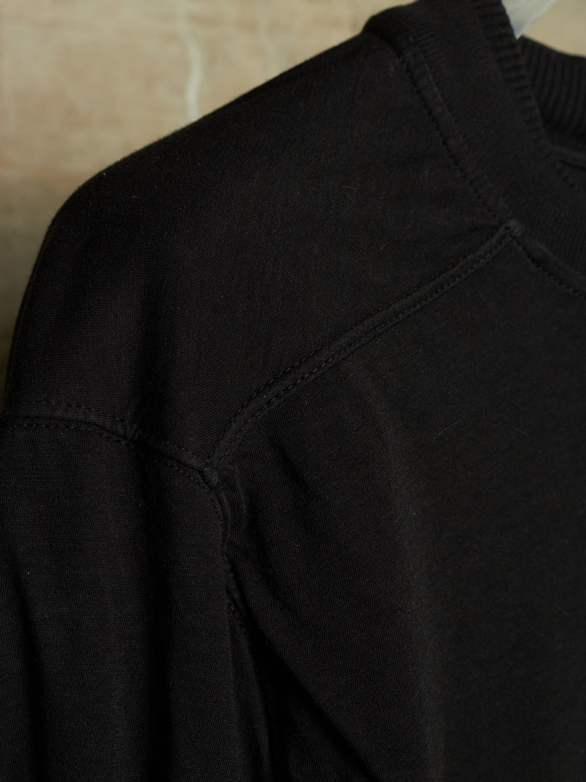 Close-up detail of a black knit crewneck sweater, showing the shoulder seam, ribbed collar, and fine fabric texture.