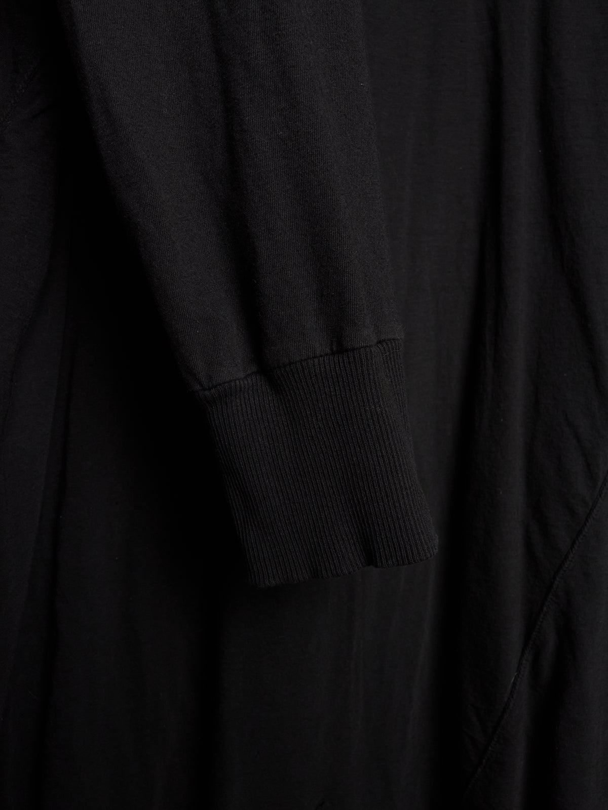 Close-up of a black long-sleeve garment with a ribbed cuff, showing soft fabric folds and texture.