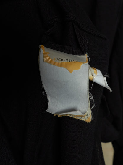 A close-up of a black garment with a small white fabric patch attached near the shoulder, featuring yellow trim and partial text reading 'MADE IN ITALY'.