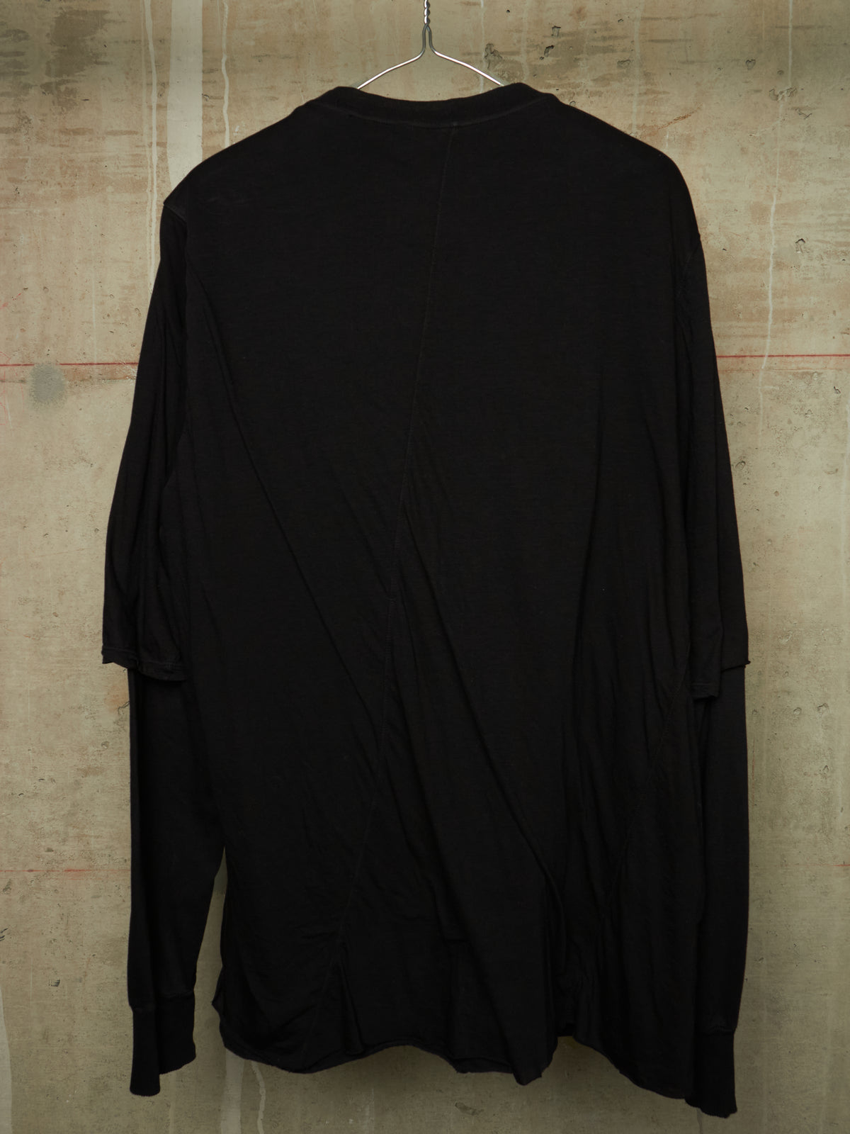 A black long-sleeve top hanging on a metal hanger against a textured concrete wall.