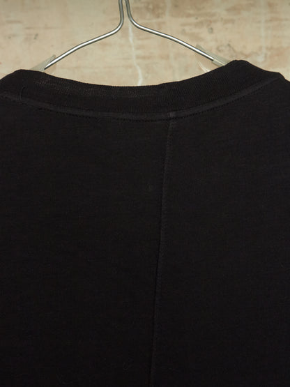 Close-up of the back of a black crewneck sweatshirt hanging on a metal hanger against a light beige textured wall.