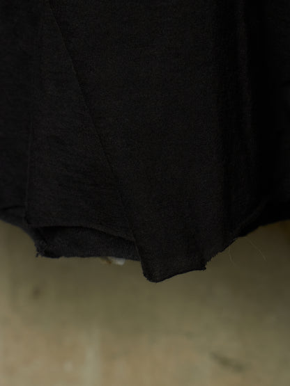 A close-up of a black fabric garment, showing the texture and hem of the material against a neutral beige background.