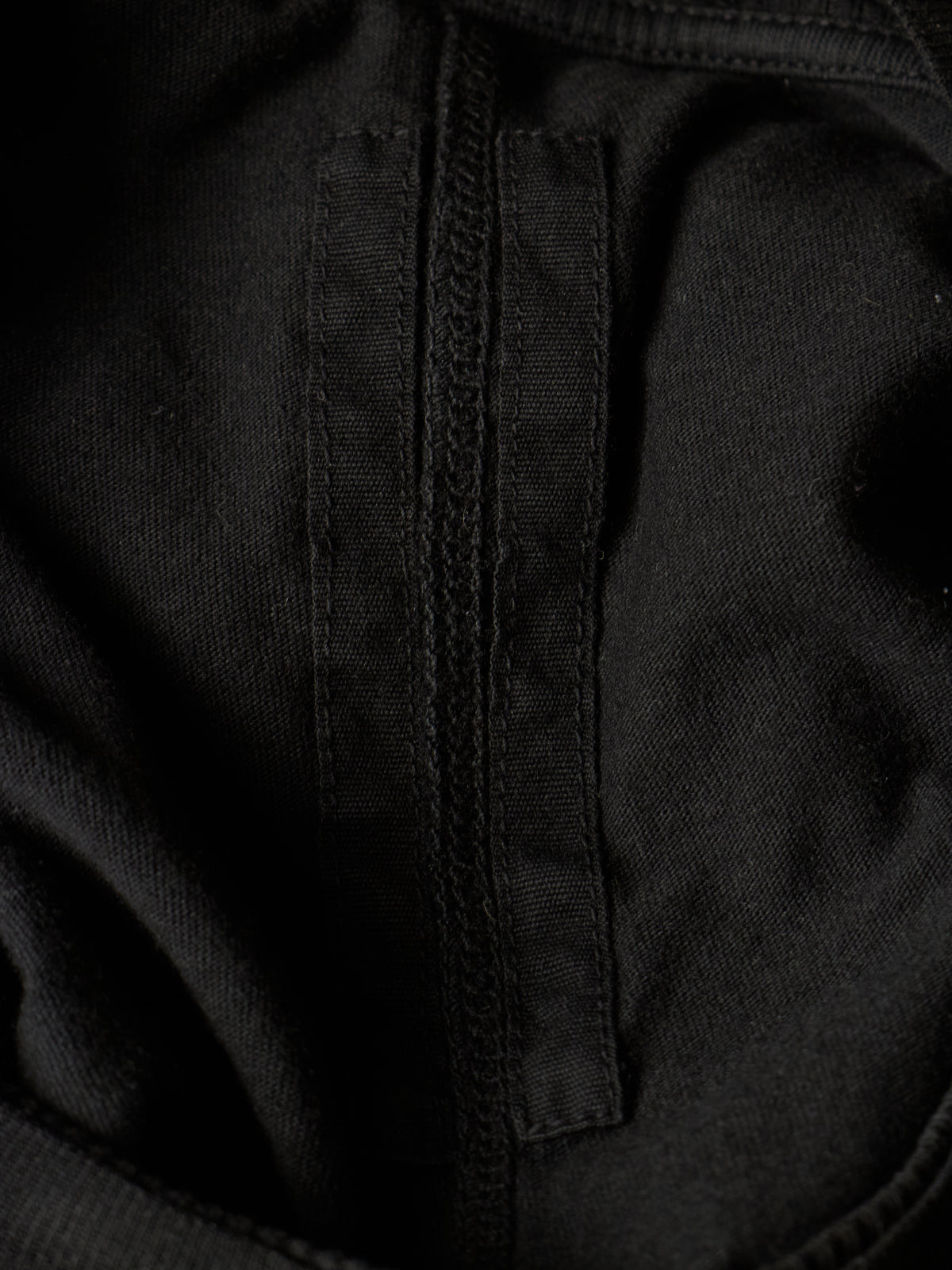 Close-up detail of a black fabric garment showing a vertical stitched seam and textured woven material.