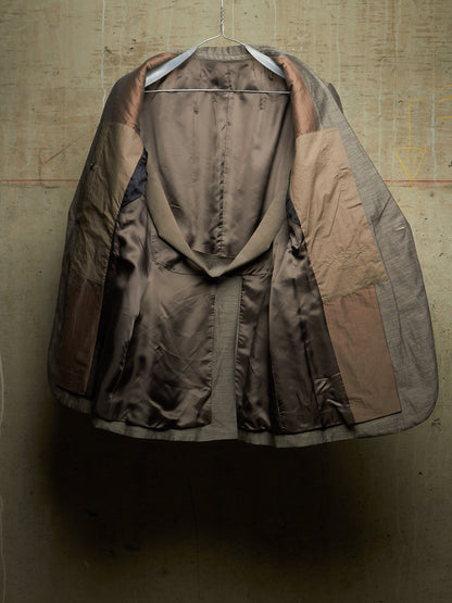 A vintage patchwork coat with a brown and beige satin-like exterior, hanging on a metal hanger against a textured concrete wall.