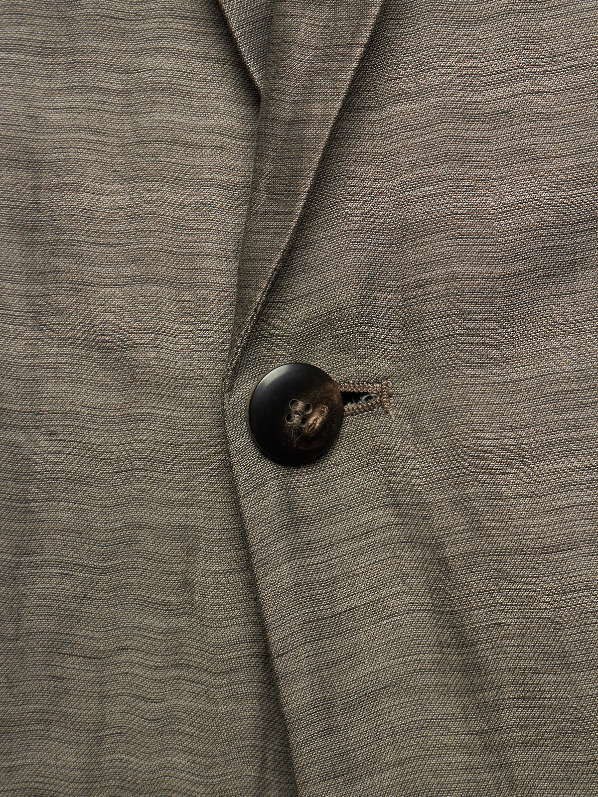 Close-up of a textured gray wool-blend blazer with a dark brown button and a small embroidered detail near the collar.