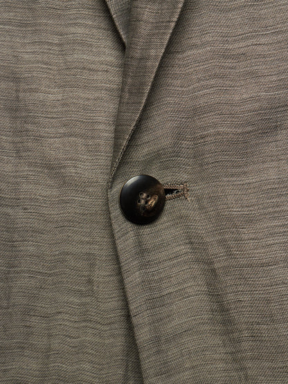 Close-up of a textured gray wool-blend blazer with a dark brown button and a small embroidered detail near the collar.