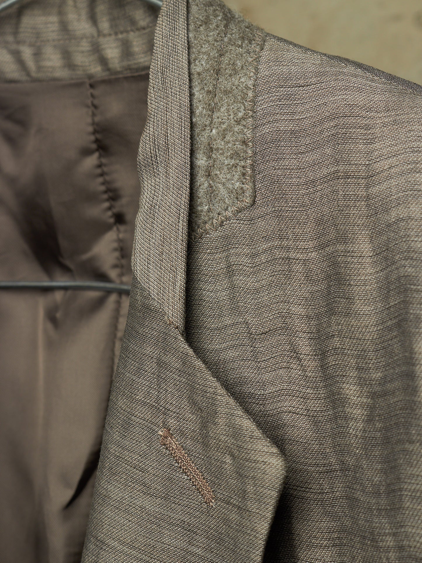 Close-up detail of a textured tweed blazer in taupe-brown and gray, showing the lapel, inner lining, and fabric weave.