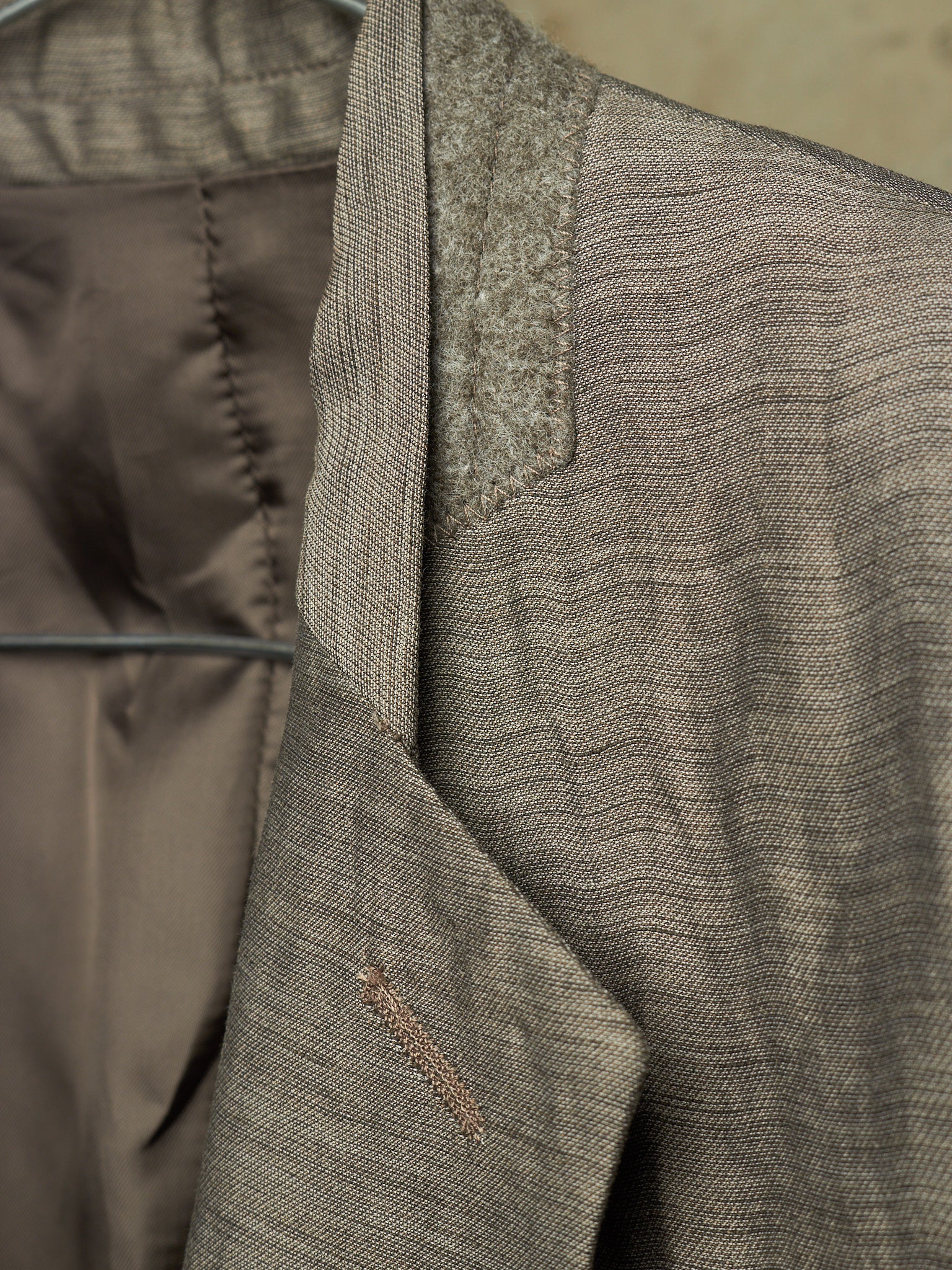Close-up detail of a textured tweed blazer in taupe-brown and gray, showing the lapel, inner lining, and fabric weave.