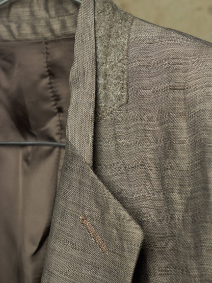 Close-up detail of a textured tweed blazer in taupe-brown and gray, showing the lapel, inner lining, and fabric weave.