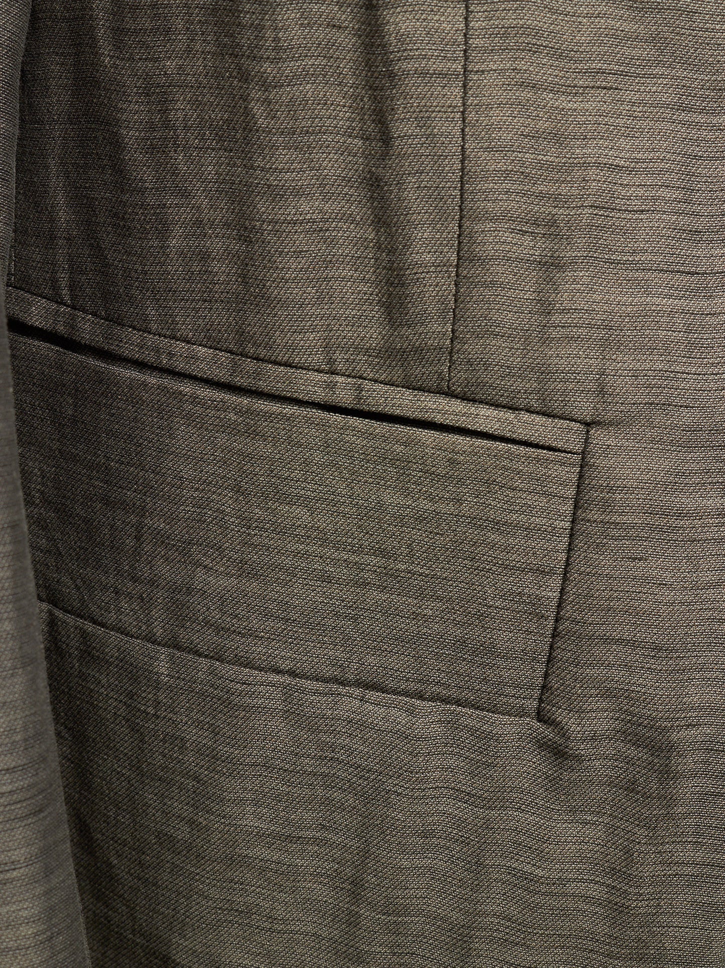 Close-up of a textured gray fabric jacket with a single welt pocket and fine woven horizontal lines.