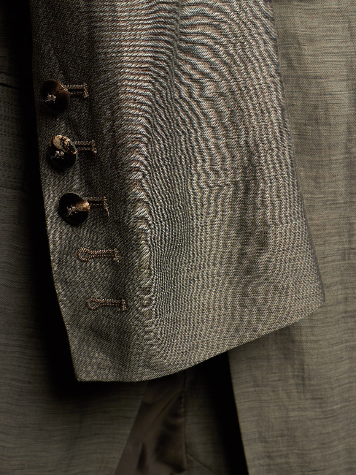 Close-up detail of a textured gray suit jacket showing the buttoned lapel with dark buttons and the fine fabric weave.