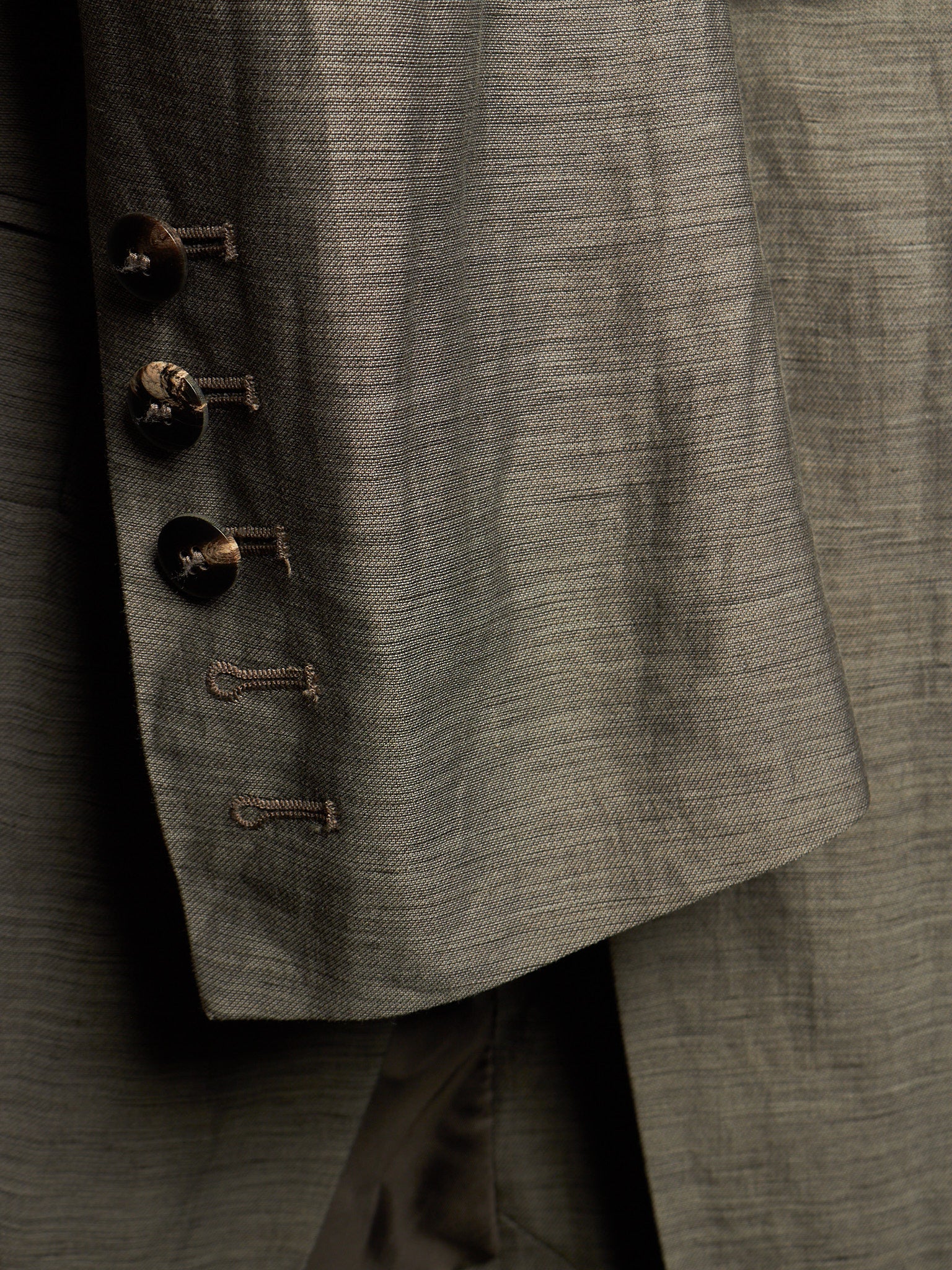 Close-up detail of a textured gray suit jacket showing the buttoned lapel with dark buttons and the fine fabric weave.