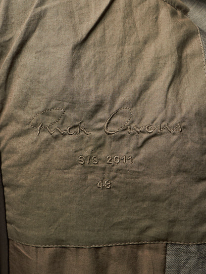 Close-up of a textured olive green fabric surface with embroidered script reading 'Rick Owens' and smaller stitched text 'STS. 2011' and '48'.
