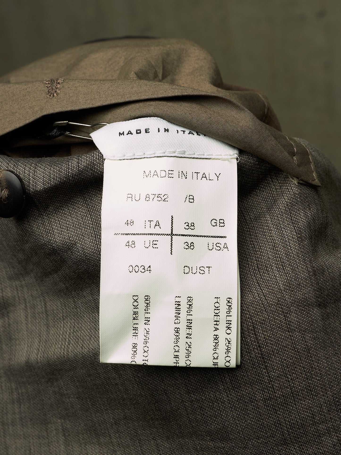 Close-up of a garment's interior label reading 'MADE IN ITALY' with size and country codes, attached to a dark brown textured fabric.