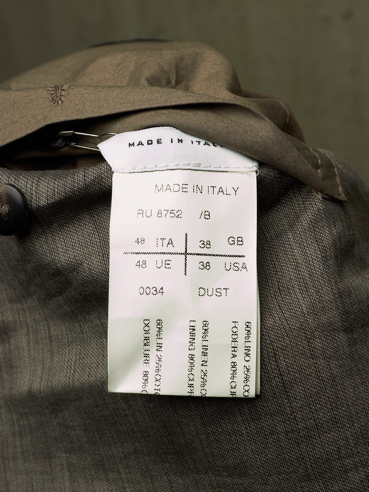 Close-up of a garment's interior label reading 'MADE IN ITALY' with size and country codes, attached to a dark brown textured fabric.