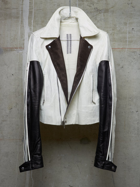 White leather jacket with black accents on a mannequin against a concrete wall.