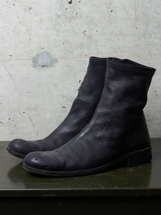 Pair of black leather boots on a textured surface with a concrete wall background