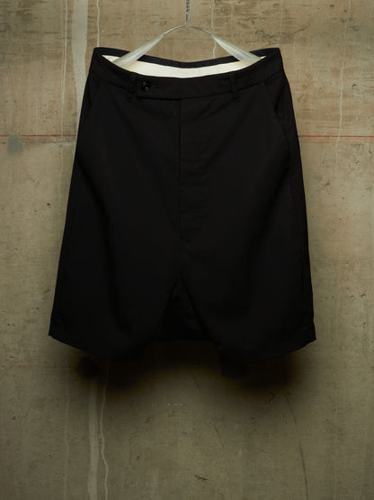 Black shorts hanging on a white hanger against a textured concrete wall.