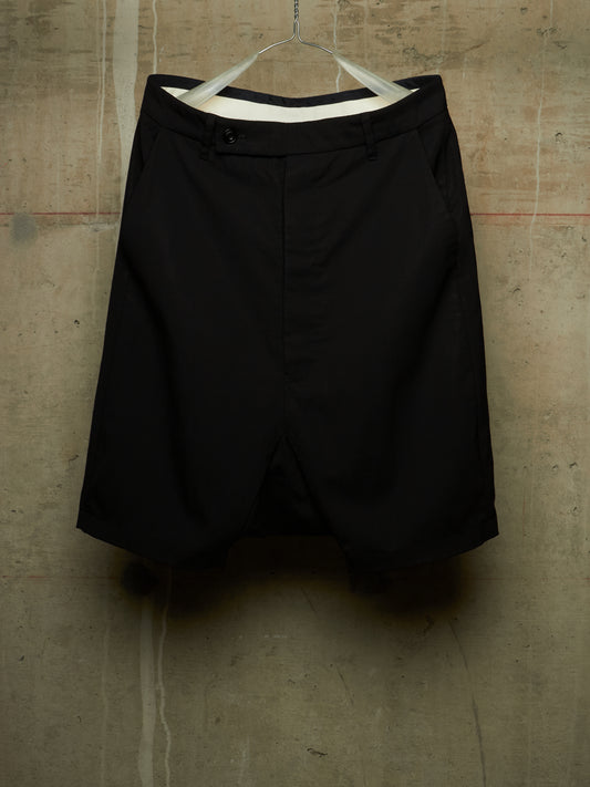 Black shorts hanging on a white hanger against a textured concrete wall.