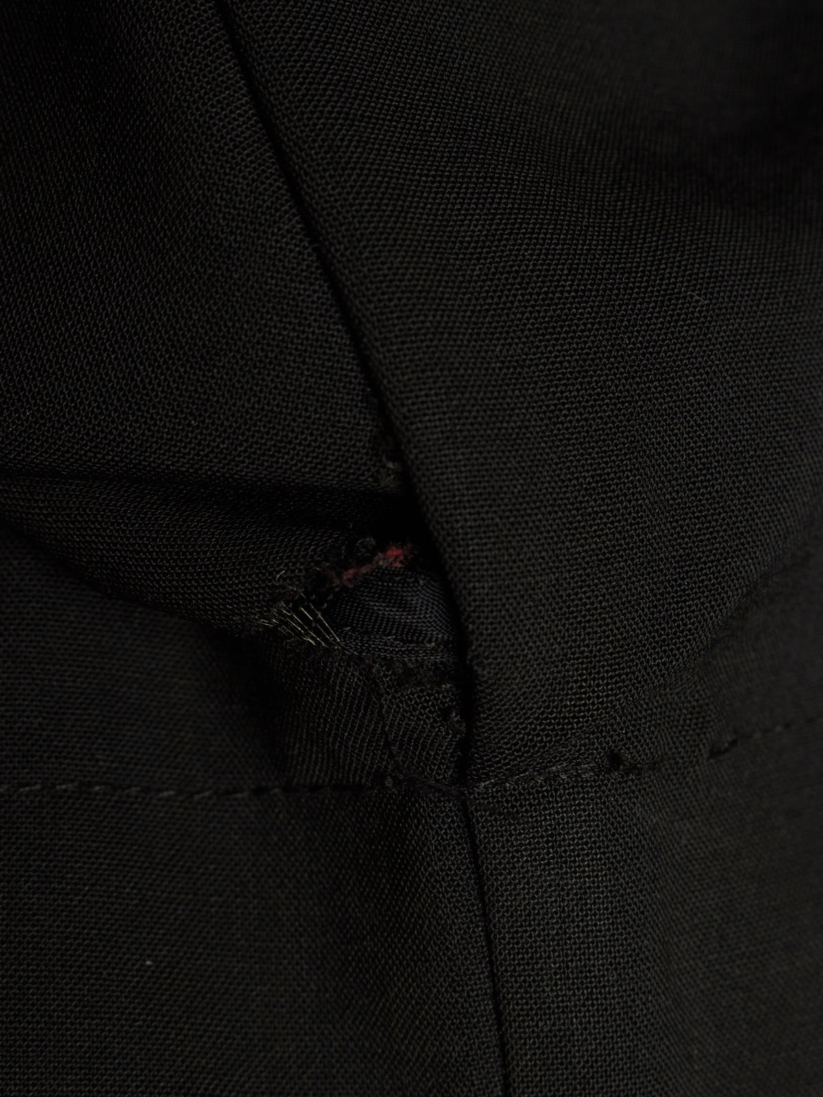 Close-up of a black woven fabric garment with a small visible red thread detail near a seam.