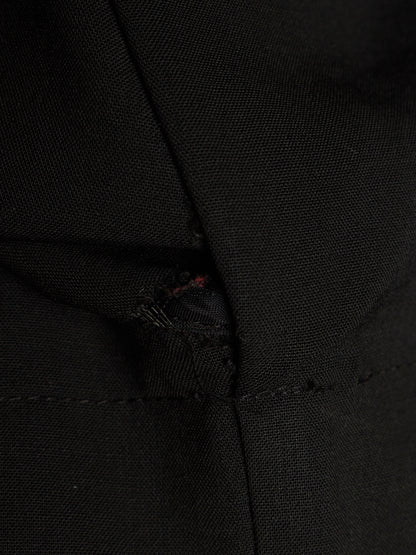 Close-up of a black woven fabric garment with a small visible red thread detail near a seam.