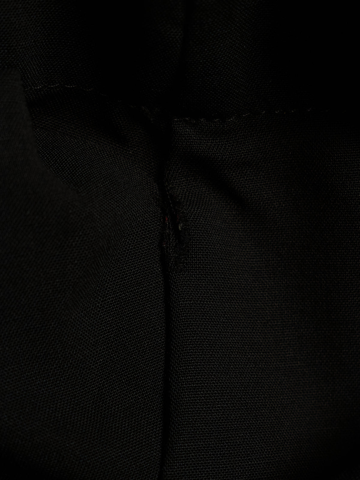 Close-up of a black textured fabric with a central seam and subtle stitched detail.