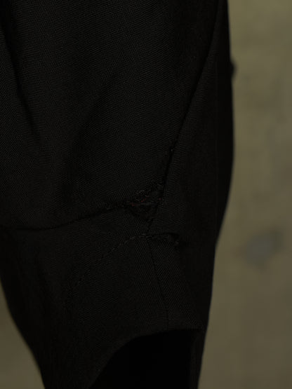 Close-up of a black textured fabric garment with a small distressed tear detail near the center, set against a dark neutral background.
