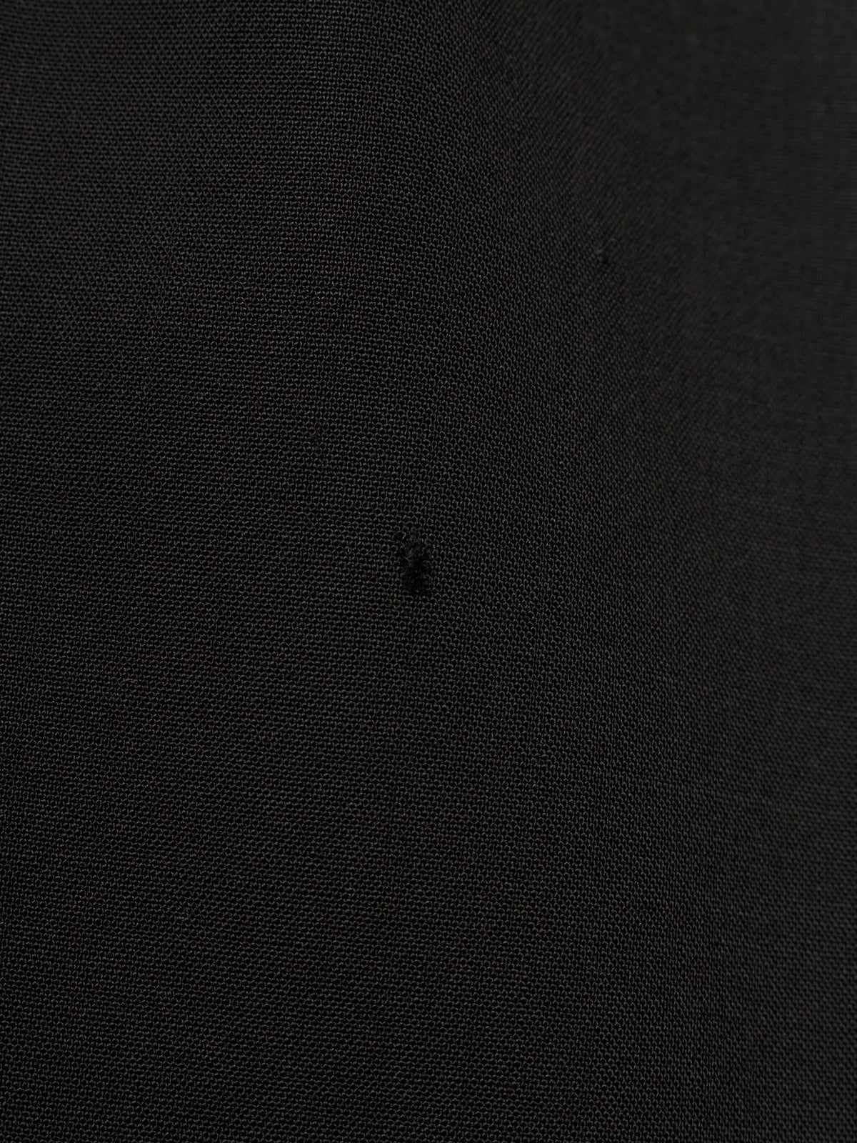 A close-up of a black textured fabric surface with a tiny dark embroidered logo in the center.