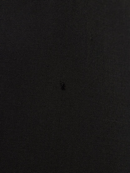 A close-up of a black textured fabric surface with a tiny dark embroidered logo in the center.
