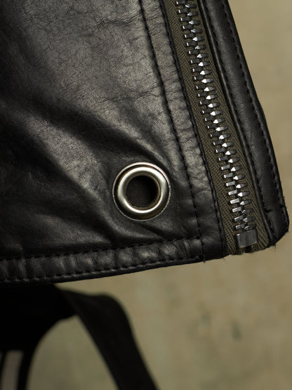 Close-up detail of a black leather jacket showing a silver metal grommet and a dark zipper with silver teeth.