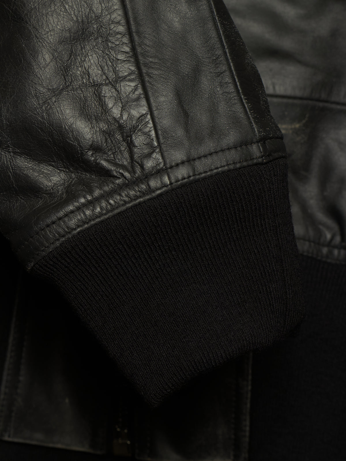 Close-up detail of a black leather jacket sleeve with a ribbed black knit cuff.