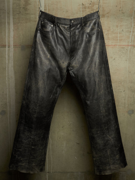 Distressed black leather pants hanging against a textured concrete wall.