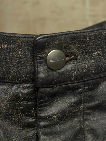 Close-up of a distressed black leather garment, likely pants or shorts, showing a round metal button with the brand name 'Gian Lorenzo' engraved on it.