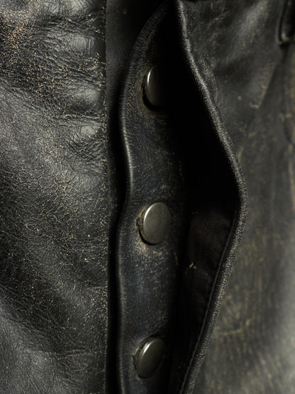 Close-up detail of a black leather jacket showing the texture of the leather, a buttoned flap, and dark metal snap buttons.