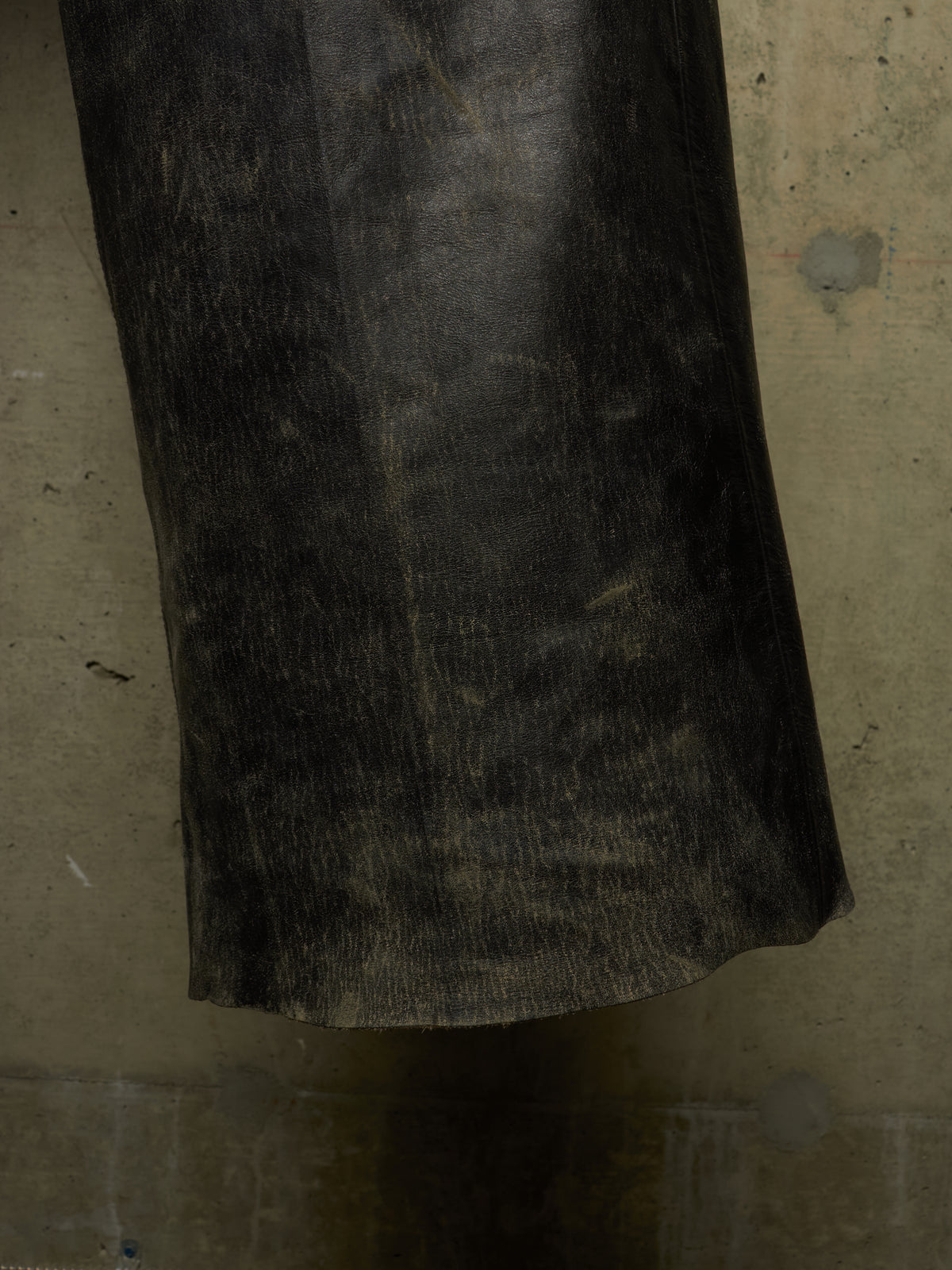 A close-up of a dark, textured black leather or faux-leather cylindrical object, possibly a boot shaft, sleeve, or handle, set against a mottled gray concrete background.