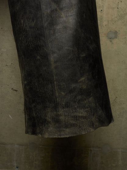 A close-up of a dark, textured black leather or faux-leather cylindrical object, possibly a boot shaft, sleeve, or handle, set against a mottled gray concrete background.